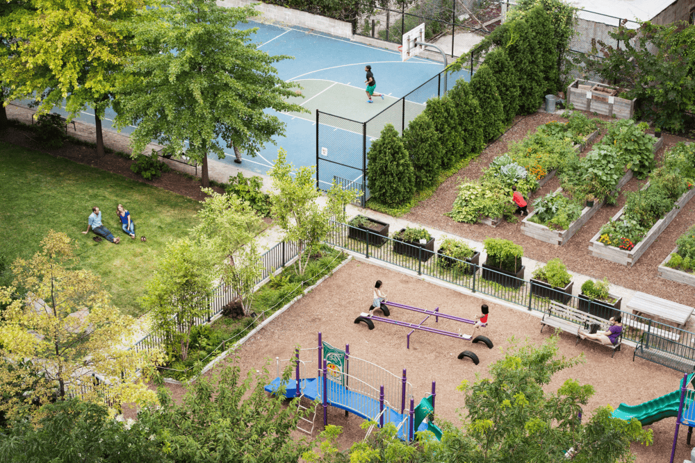An urban community garden featuring raised vegetable plots, a playground, and basketball court—all integrated within a shared landscape.