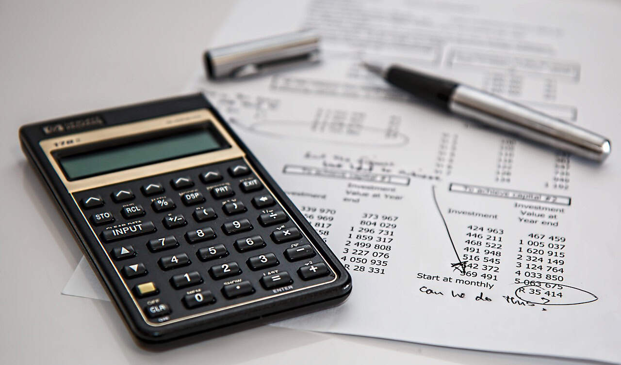 Calculator, tax forms, and a note reading ‘Need help?’ symbolizing financial services such as tax preparation, accounting, and financial support.