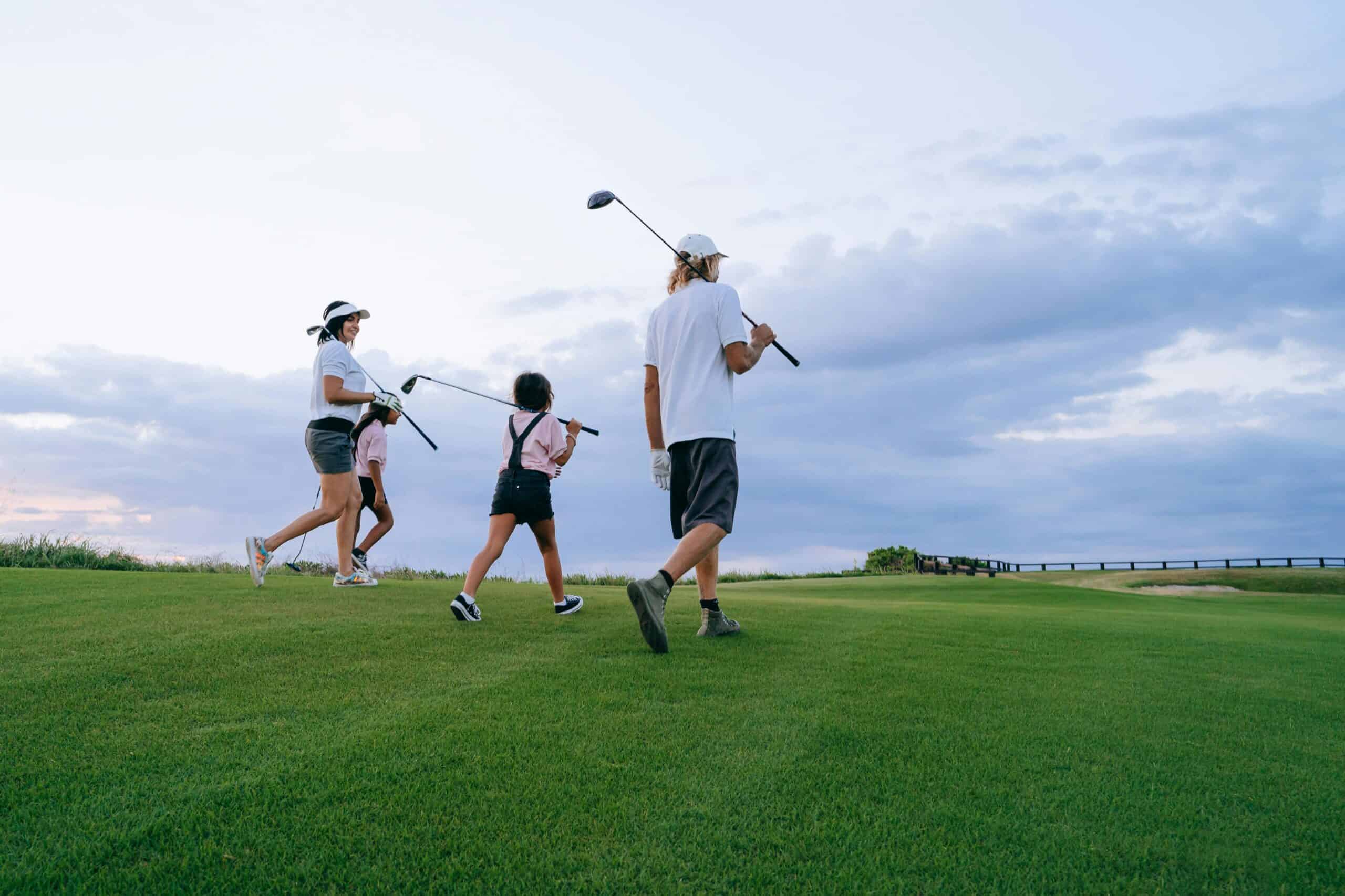 A group of people walking on a golf course carrying golf clubs under a cloudy sky.