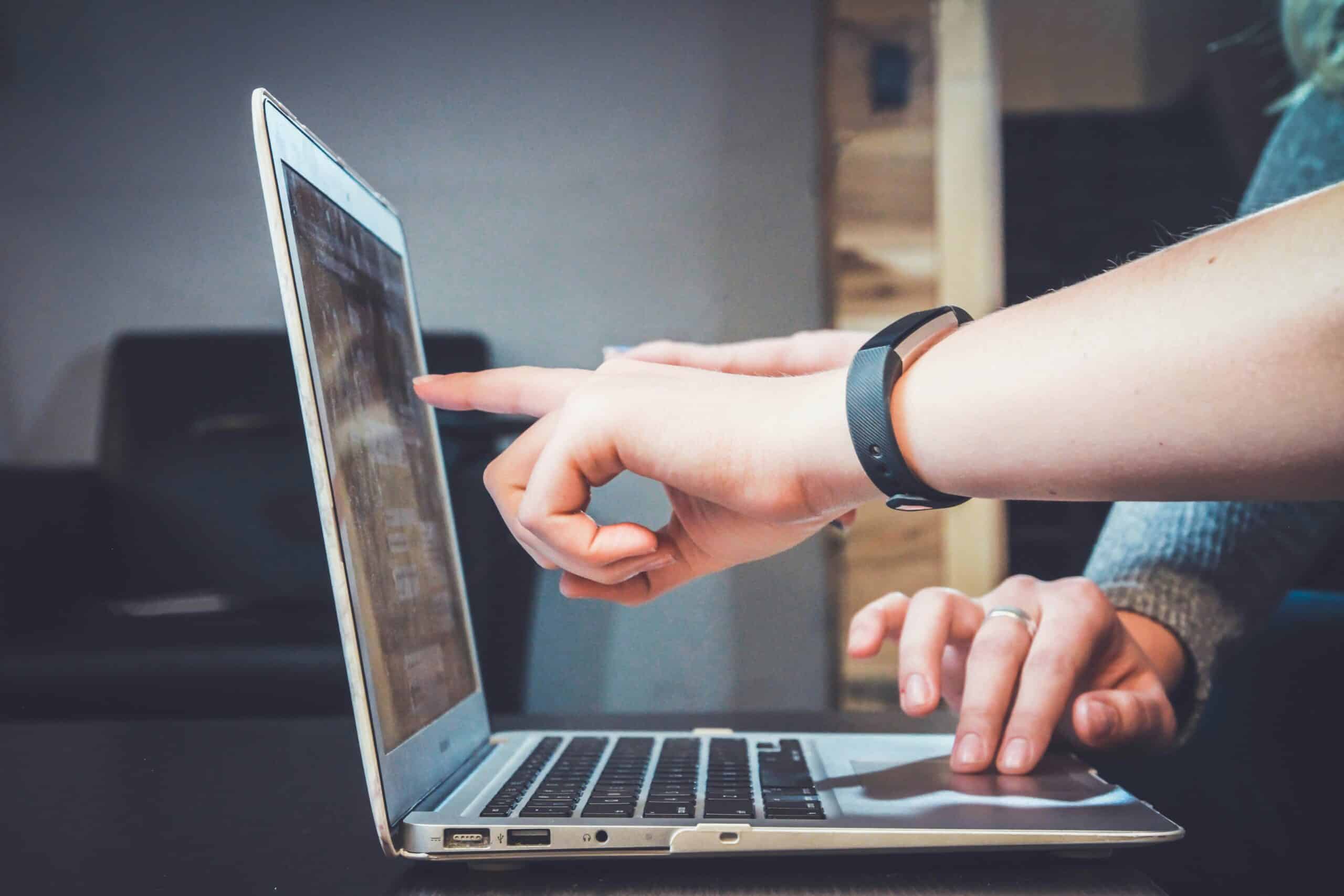 Person pointing at a laptop screen while another types.