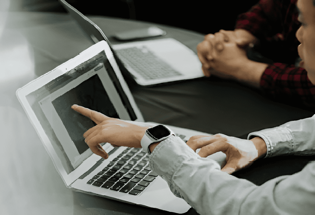 Person pointing at a laptop screen during a meeting.