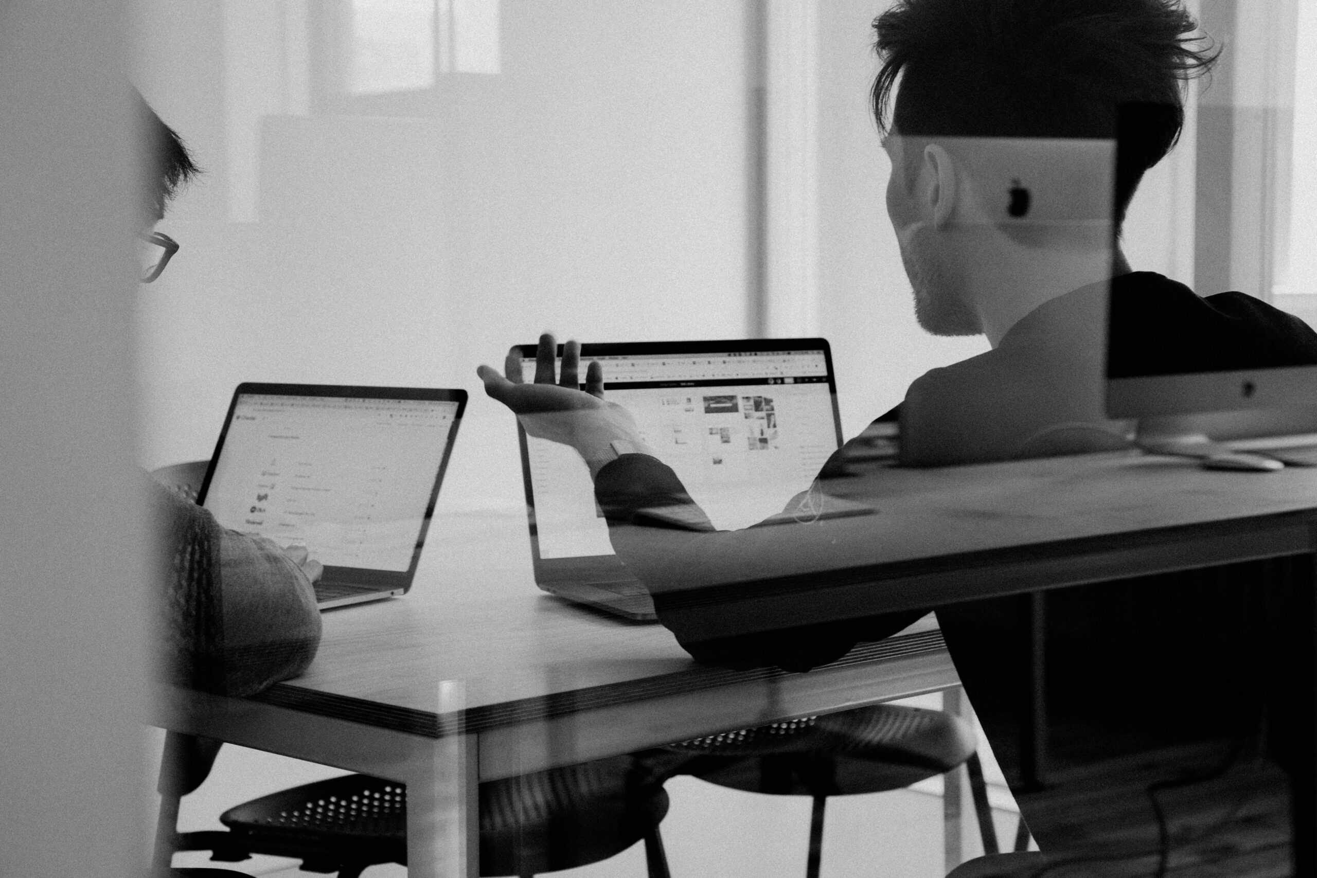 Two people working on laptops in an office meeting.