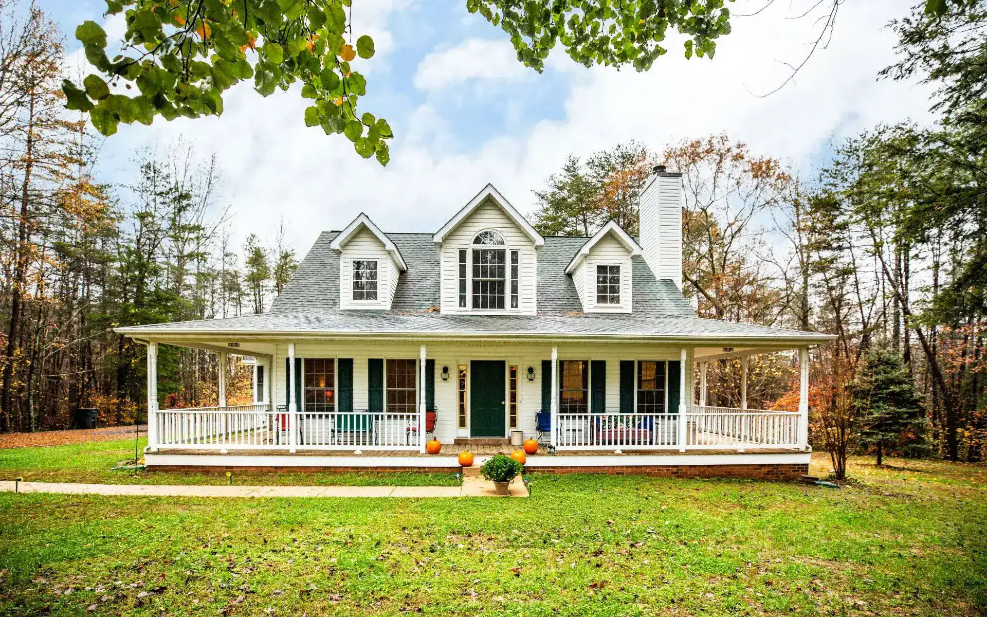Charming white farmhouse-style home in Stafford County with a wraparound porch and surrounded by trees in autumn.