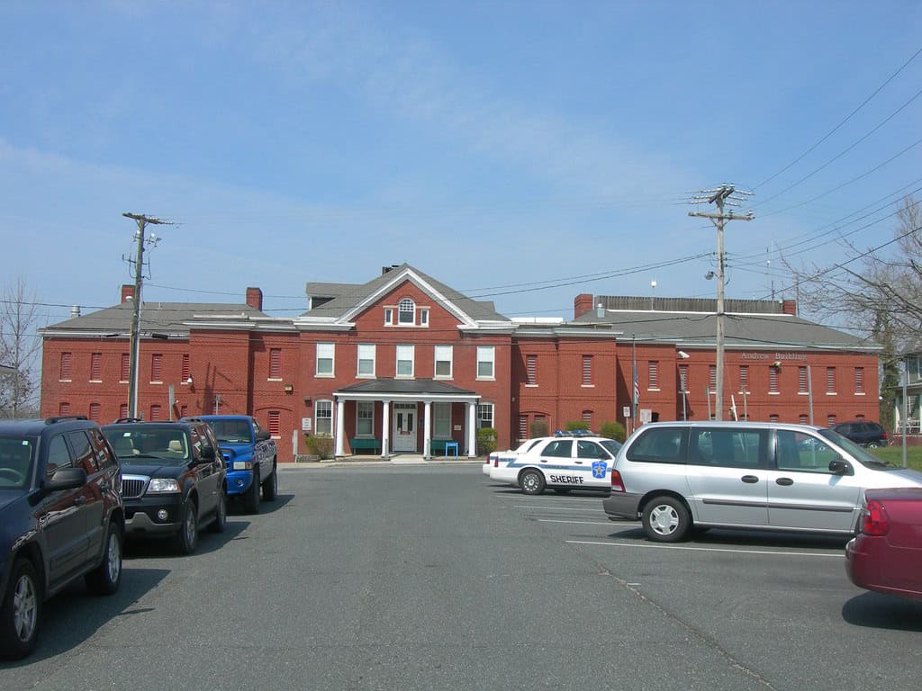 Red brick government building with central entrance and parked vehicles in front under a clear sky.
